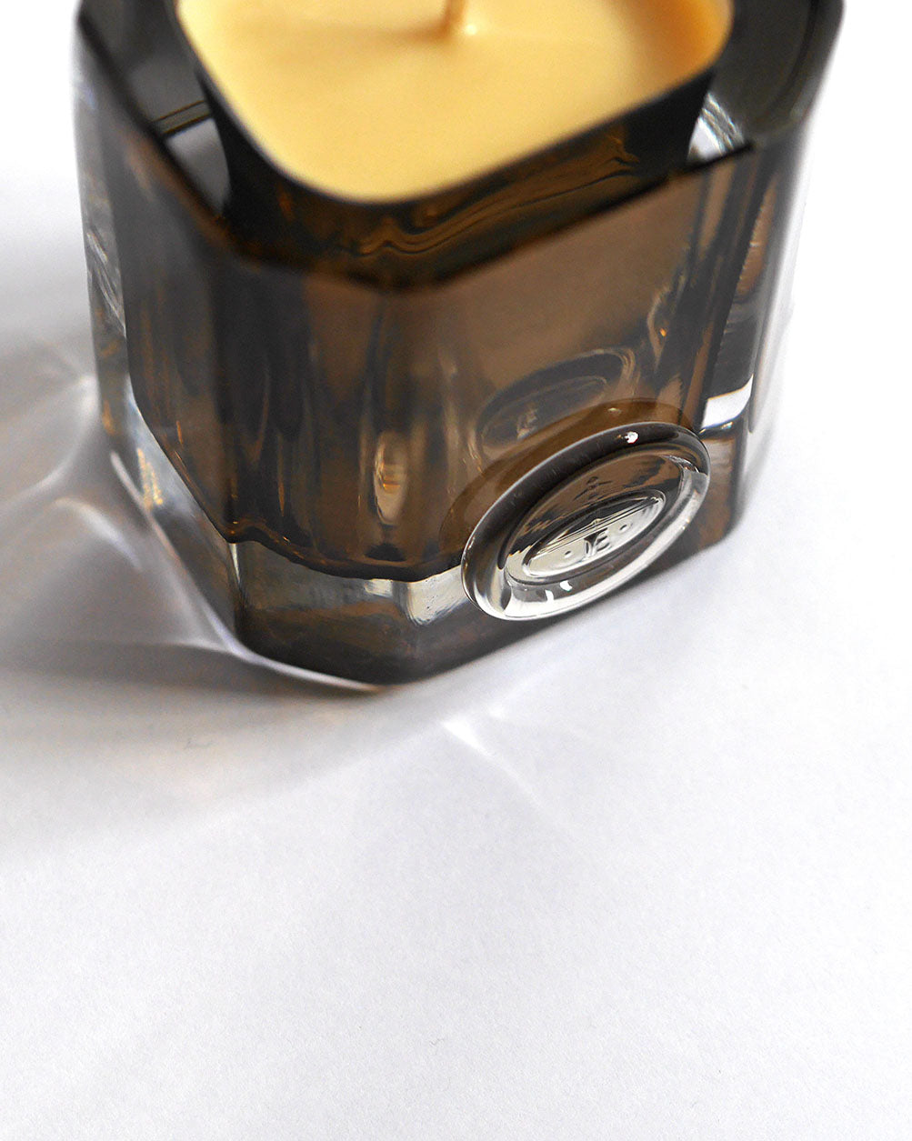 Close-up of a smoked amber glass ENYALYË vessel candle with its engraved emblem, resting on a marble surface.